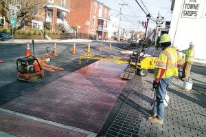 Workers give the appearance of brick to a crosswalk in downtown Stanardsville, matching the surrounding buildings’ historic brick charm. Grants have helped move the streetscape forward. (Photo provided)