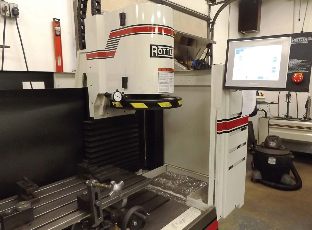 This CNC resurfacing machine can extend the life of vehicles for cities and towns. The engine part is clamped down and the diamond cutting edge travels above it while the touch screen, where the machine is programmed, extends out to the side. (Photo by Denise Fedorow)