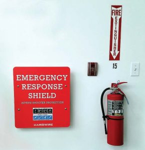 Much like a fire extinguisher, an emergency response shield can be placed in a building in case of an active shooter. They can be labeled as such, above right, or concealed as artwork or an advertisement, like this “Seacrets Hand-Crafted Gin” sign, above left. (Photo provided by Hardwire)