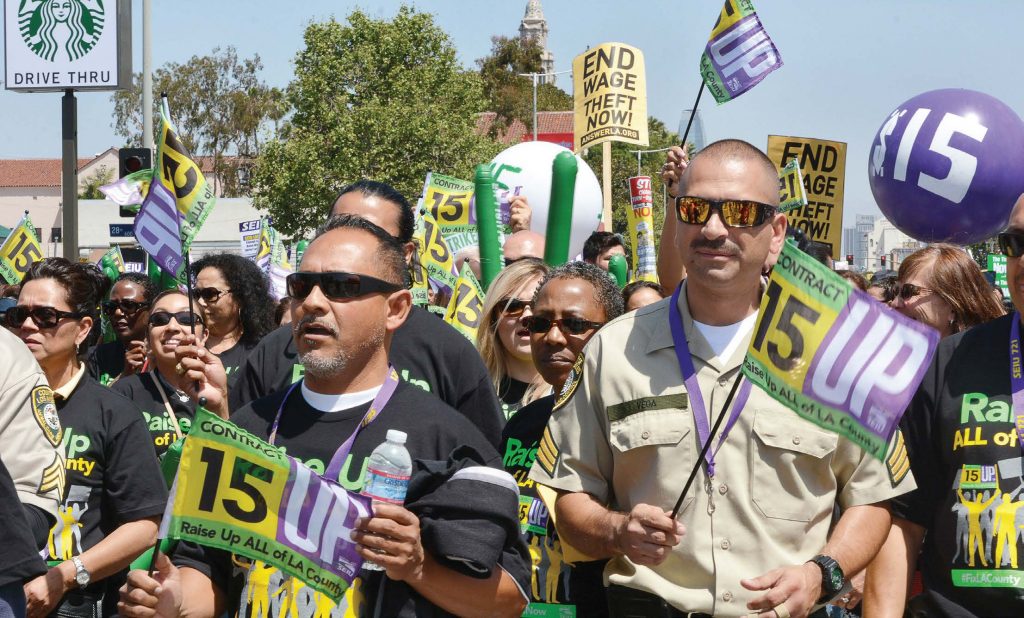 Protestors hold signs and flags advocating raising the minimum wage during a demonstration in Los Angeles on April 15, 2015. The state of California has 22 communities that have enacted minimum wage ordinances, the majority of which are on a path to $15 per hour. (Dan Holm/Shutterstock.com)