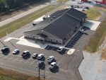 A large gray building with a black roof, surrounded by parking lot, all viewed from above.